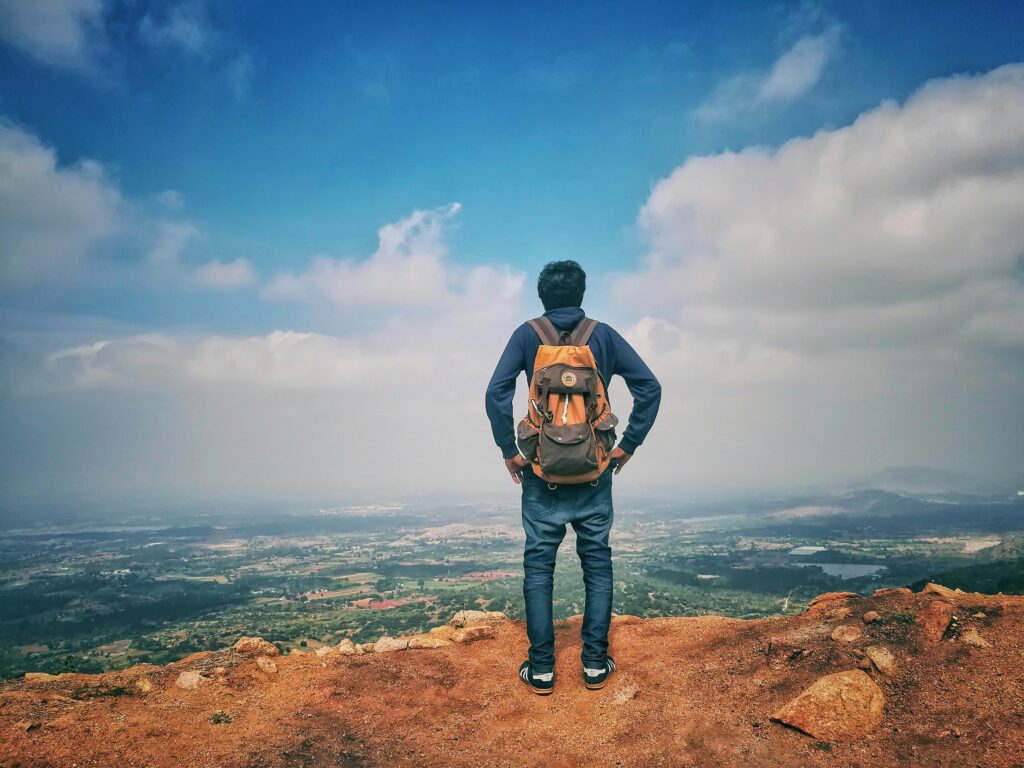 A man stands on a mountain edge appreciating the expansive scenic view below under a bright sky.